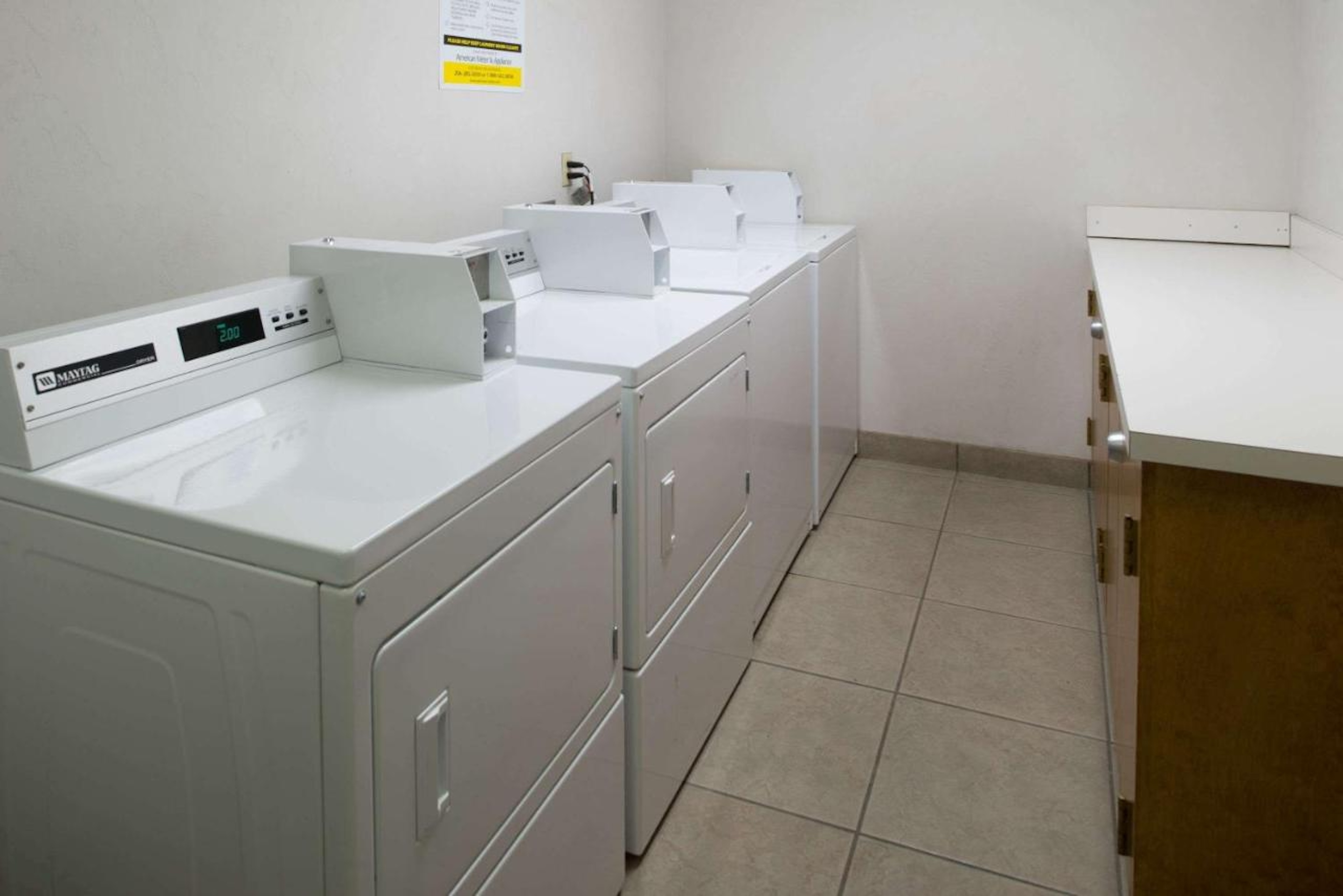 Laundry room with white Maytag washers and dryers on tiled floor.