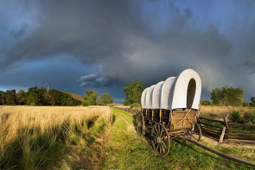 A wagon outside in a field with a blue stormy sky behind it.
