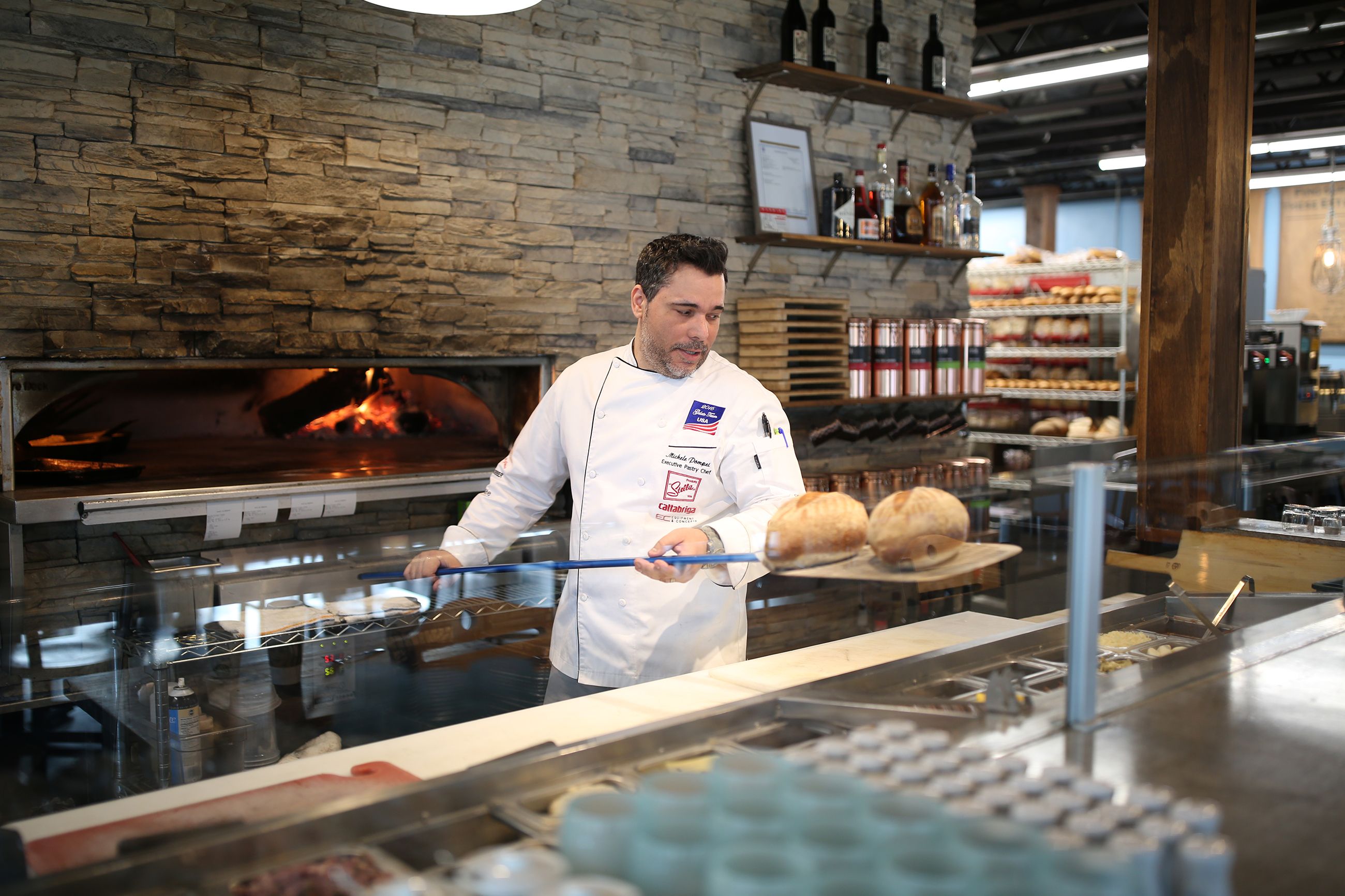 Pastry chef with fresh loaves of bread on a large wood spatula in bakery kitchen