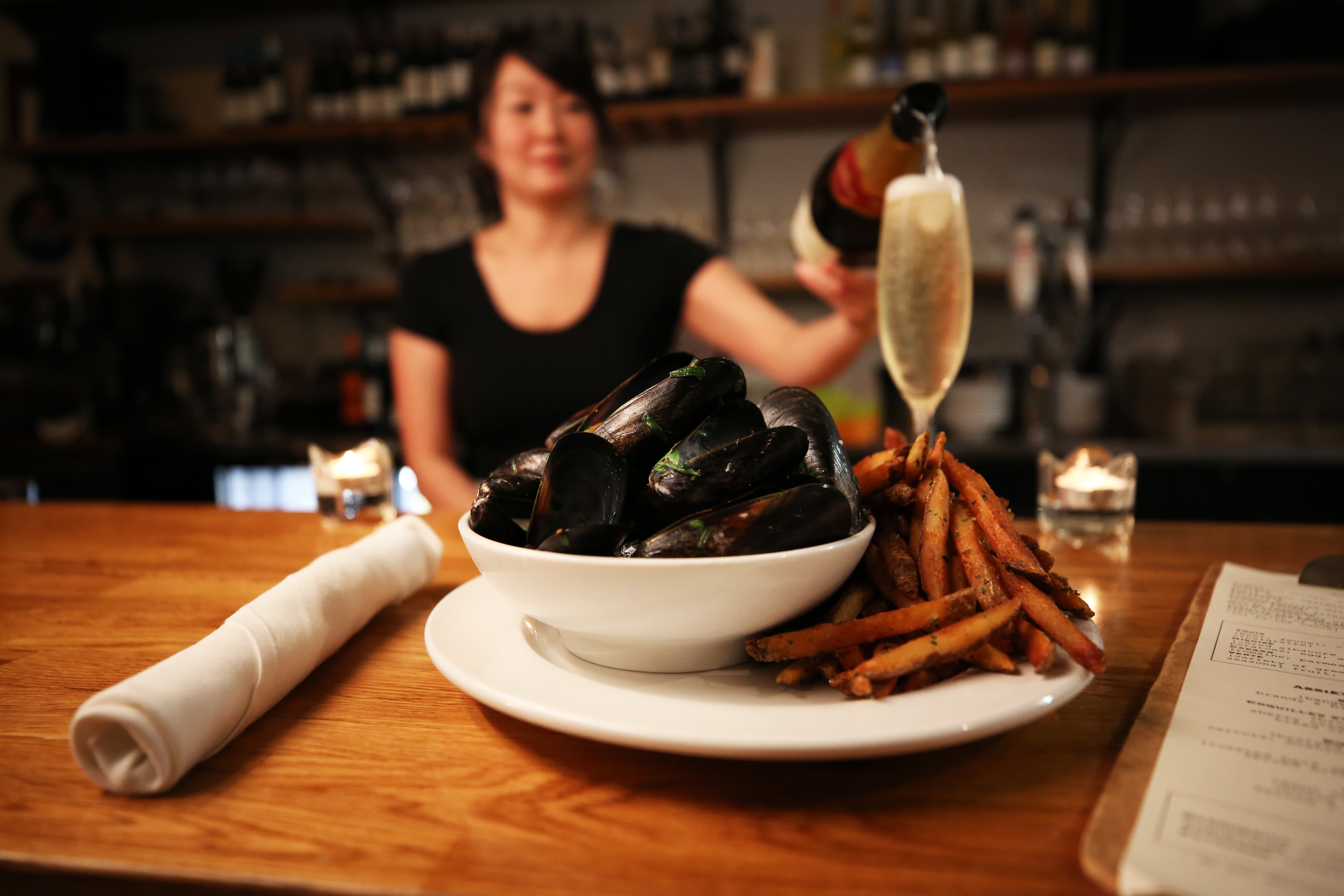 Mussels and french fries on a plate. And a bartender pouring a glass of champagne behind the bar