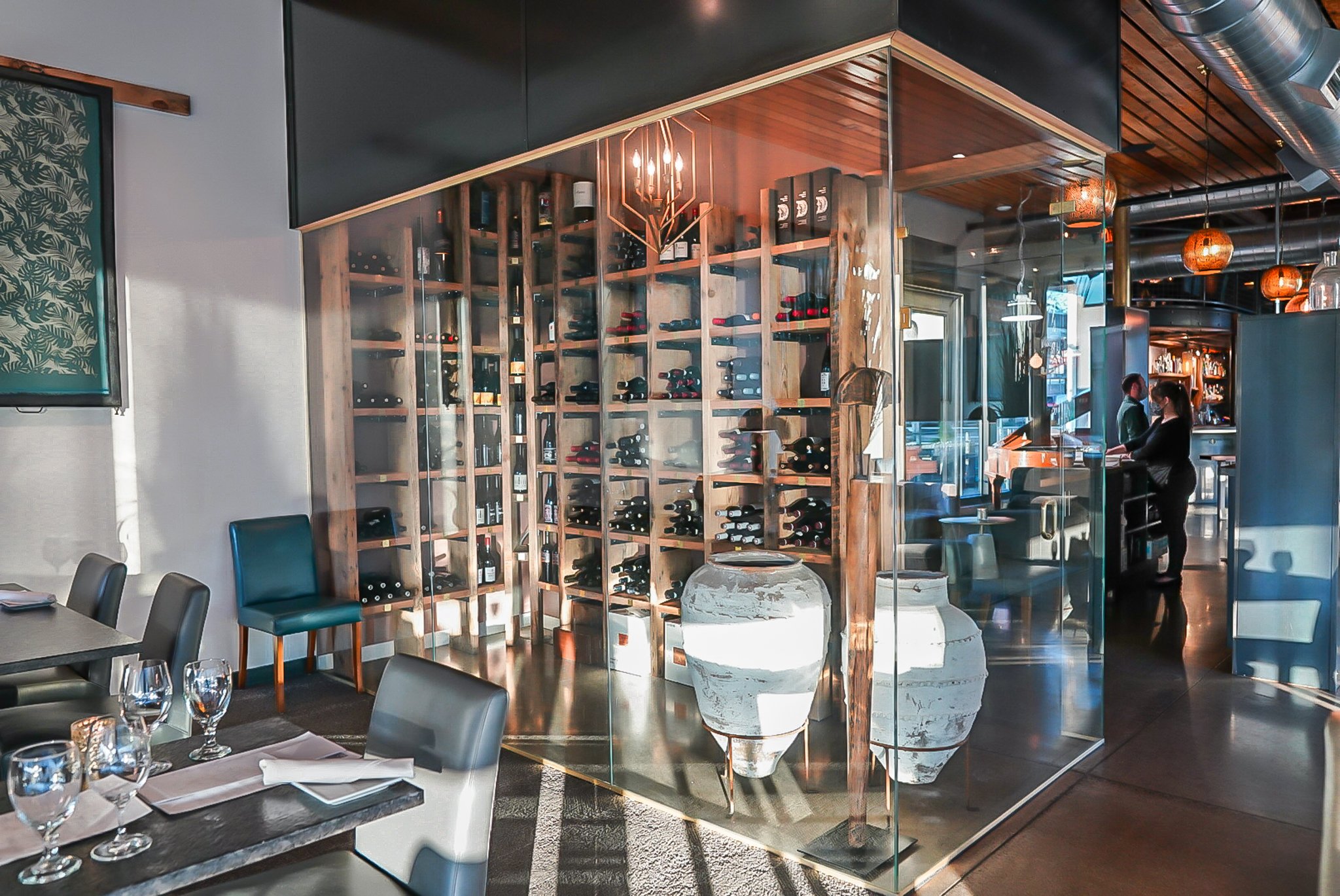 The sleek interior of TMACS features a glass-enclosed wine cellar, with stacked bottles and two large white urns.