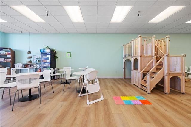 Indoor seating area with round tables and wooden climbing structure in children's center.