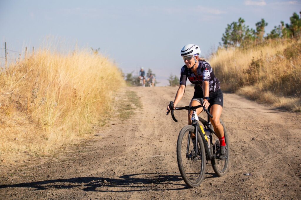 A biker biking on a dirt path that goes through a wheat field.