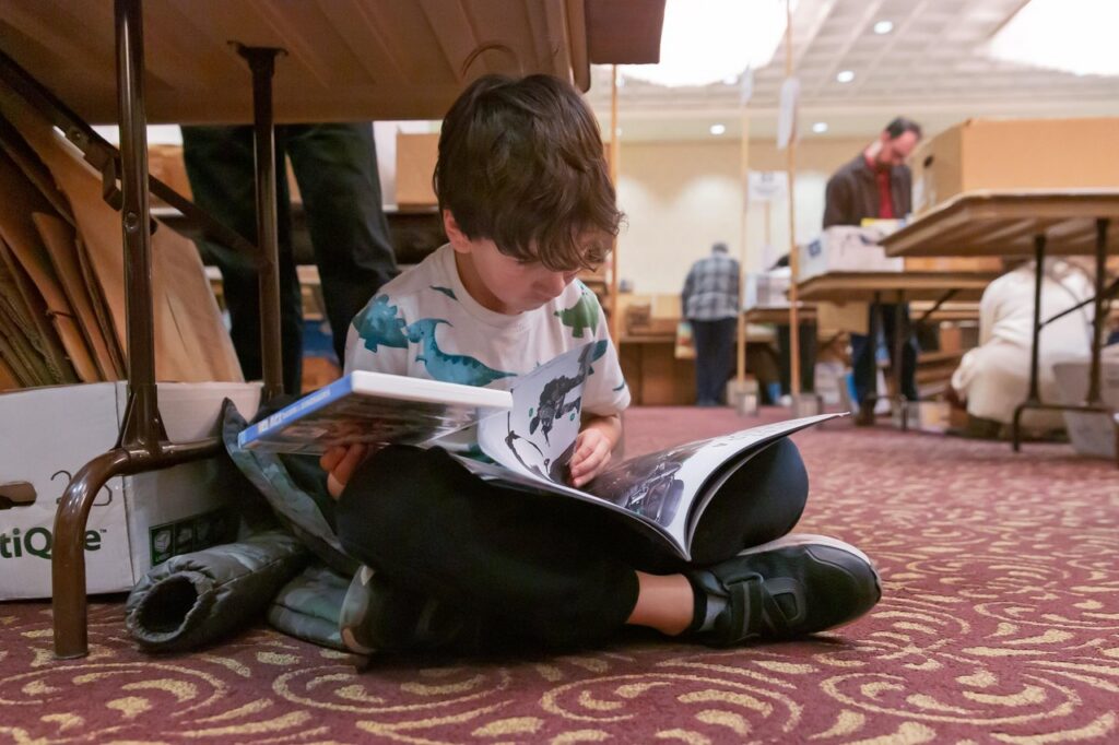 AAUW Book Sale kid reading under a table